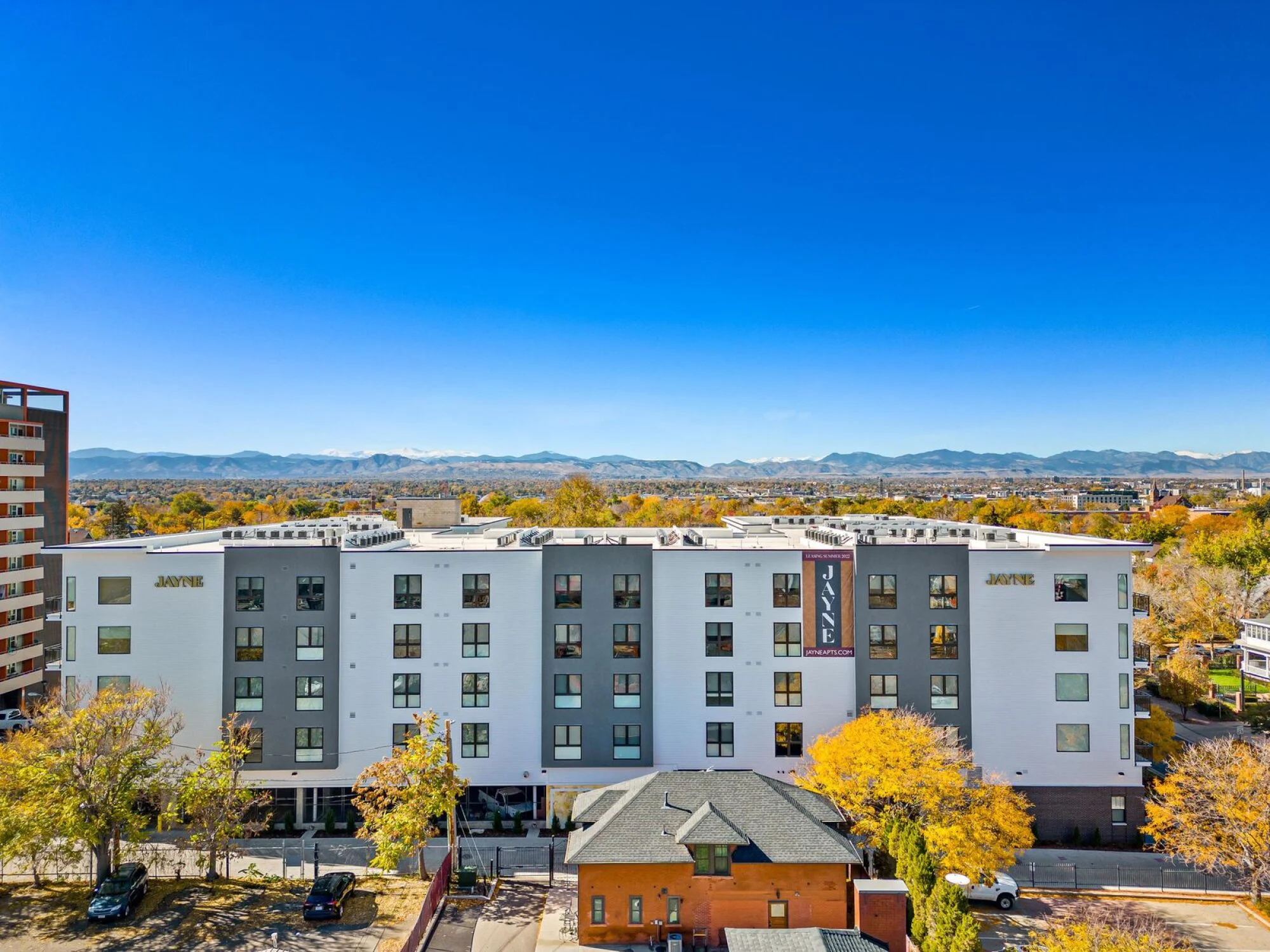 A modern apartment building labeled “JAYNE” with mountains in the background, welcoming residents home.