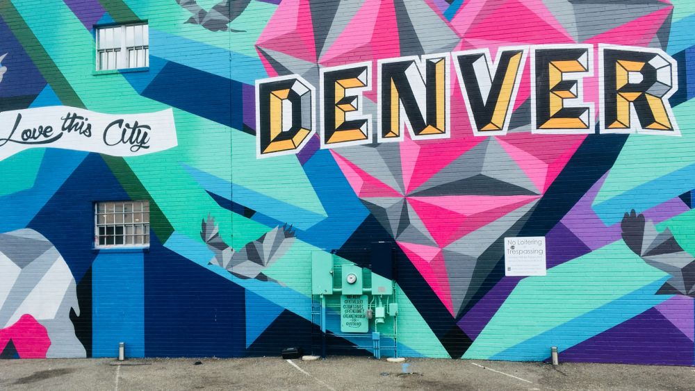 Colorful mural with geometric shapes, text reading “DENVER” and “Love this City,” painted on a building wall.