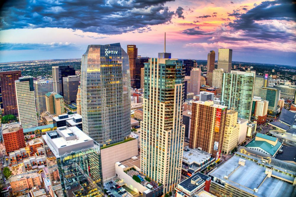 A vibrant cityscape with modern skyscrapers at sunset, under dramatic clouds, viewed from above.
